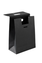 A minimalist black paper shopping bag with a flat, minimalist design, featuring a cutout handle and a small horizontal slot on the front, set against a plain white background.